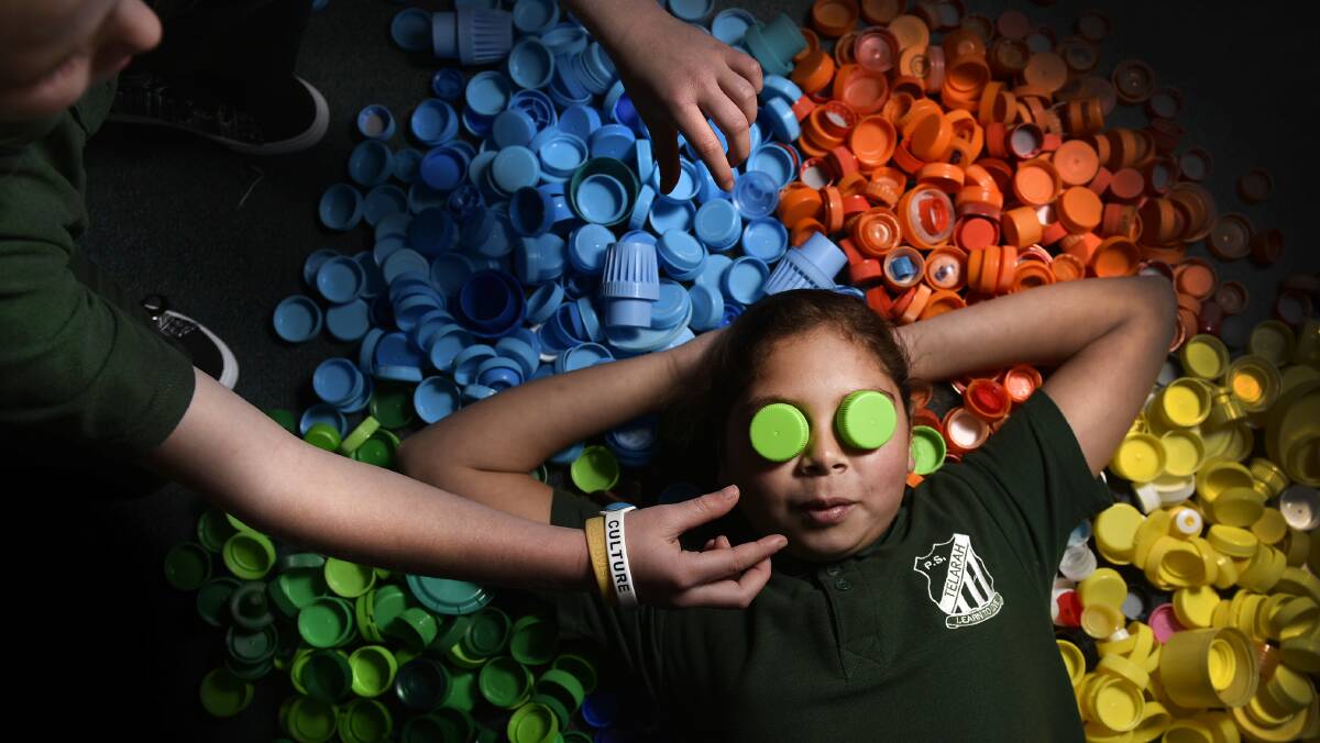 CAPPING IT OFF: Year four student Alliyra Walford relaxes in a pile of 3000 bottlecaps on the floor of Telarah Public School. Picture: Perry Duffin