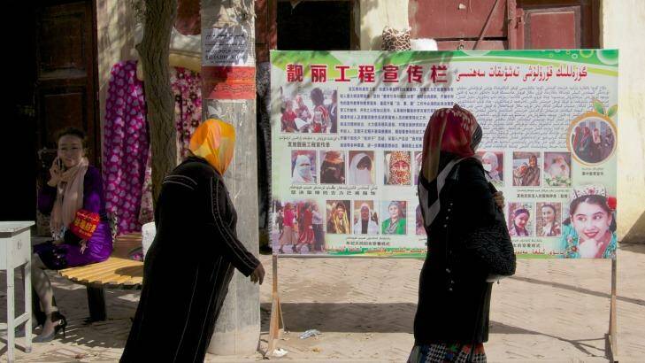 Two women pass a billboard in Kashgar instructing Uighurs not to wear religious garments that cover their face. Photo: Sanghee Liu 
