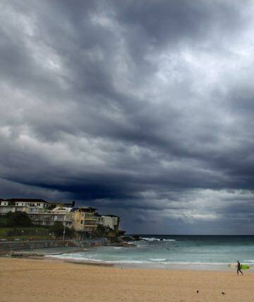 A lone surfer on Bondi Beach Christmas eve as ominous clouds signal the approaching weather system that will bring storms and another dangerous surf conditions to Sydney. Photo: Dallas Kilponen