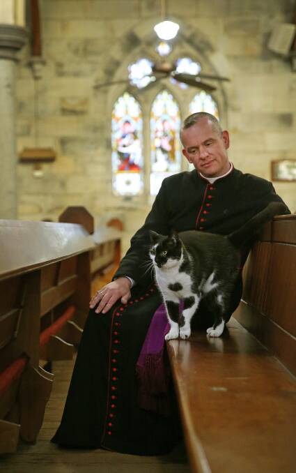 AT HOME: Priest Father David Battrick with Kyrie, one of the cats-in-residence at St Peter's Anglican Church, East Maitland. Pictures: Marina Neil