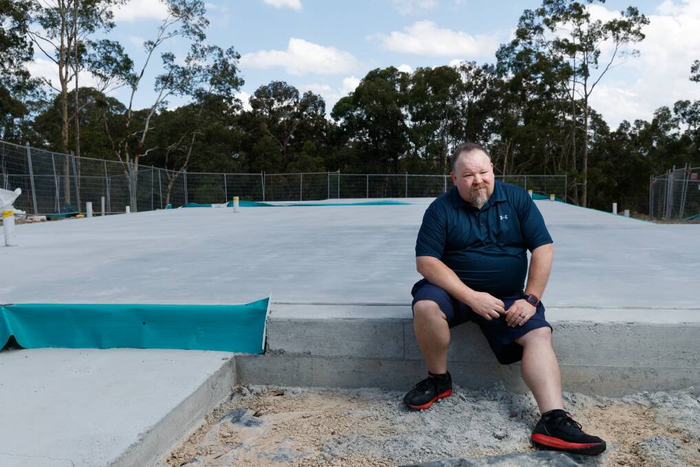 Nathan Whyte-Southcombe sitting on the concrete slab where his new home should be standing at the Heritage Parc development in Rutherford. Picture: Max Mason-Hubers