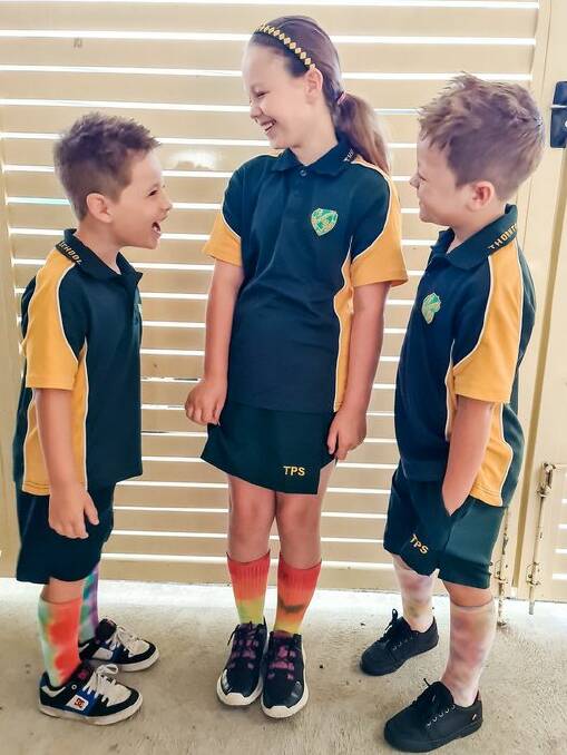 RAINBOWS: Hallie and her younger brothers wearing their Hallie Project socks to school. Picture: Supplied.