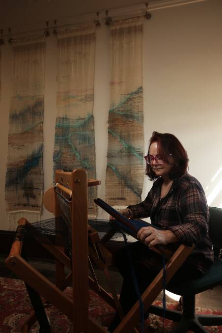 ARTIST AT WORK: Inaugural artist in residence, Ellen Howell, using a loom with her woven artwork 'Five Rivers' displayed on the wall. Picture: Simone De Peak.