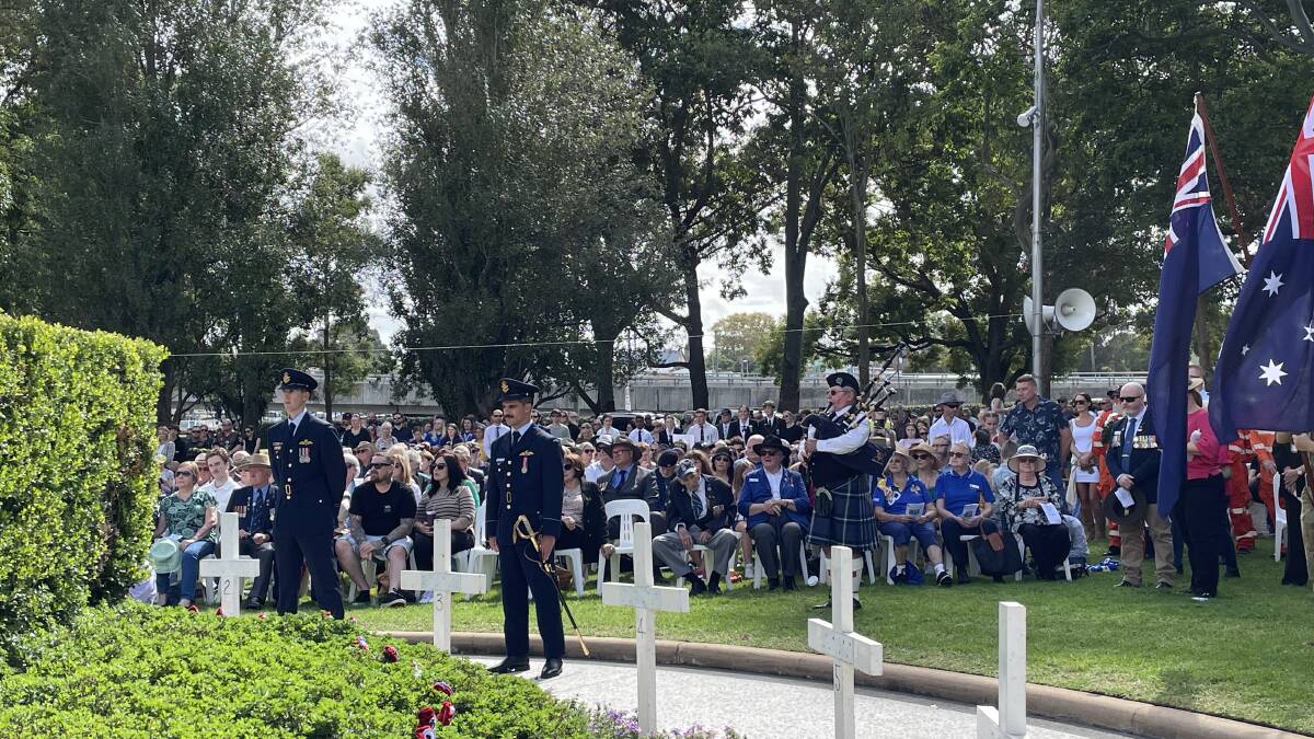 Members of No.2 Squadron RAAF Base Williamtown and City of Maitland Pipes and Drums bagpiper Robbie Cheetham stand before the huge crowd at Maitland Park. Picture by Chloe Coleman