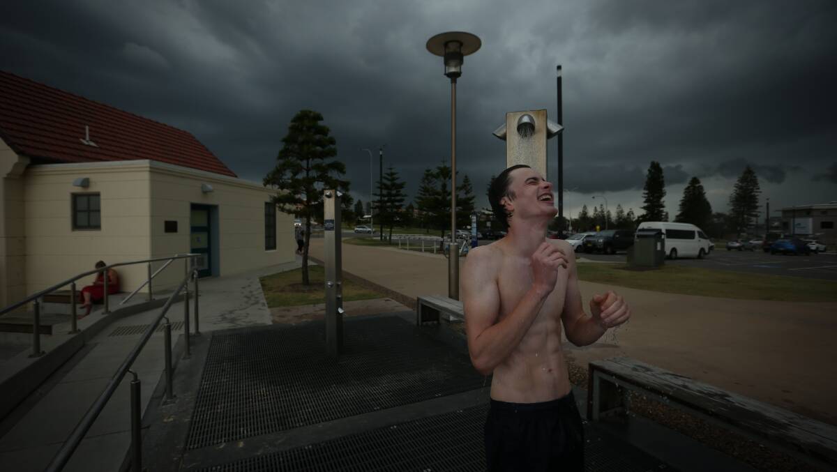 RAINING DOWN: Tom Merrett washes off after a swim at Nobbys as a storm front rolls in. Picture: Simone De Peak