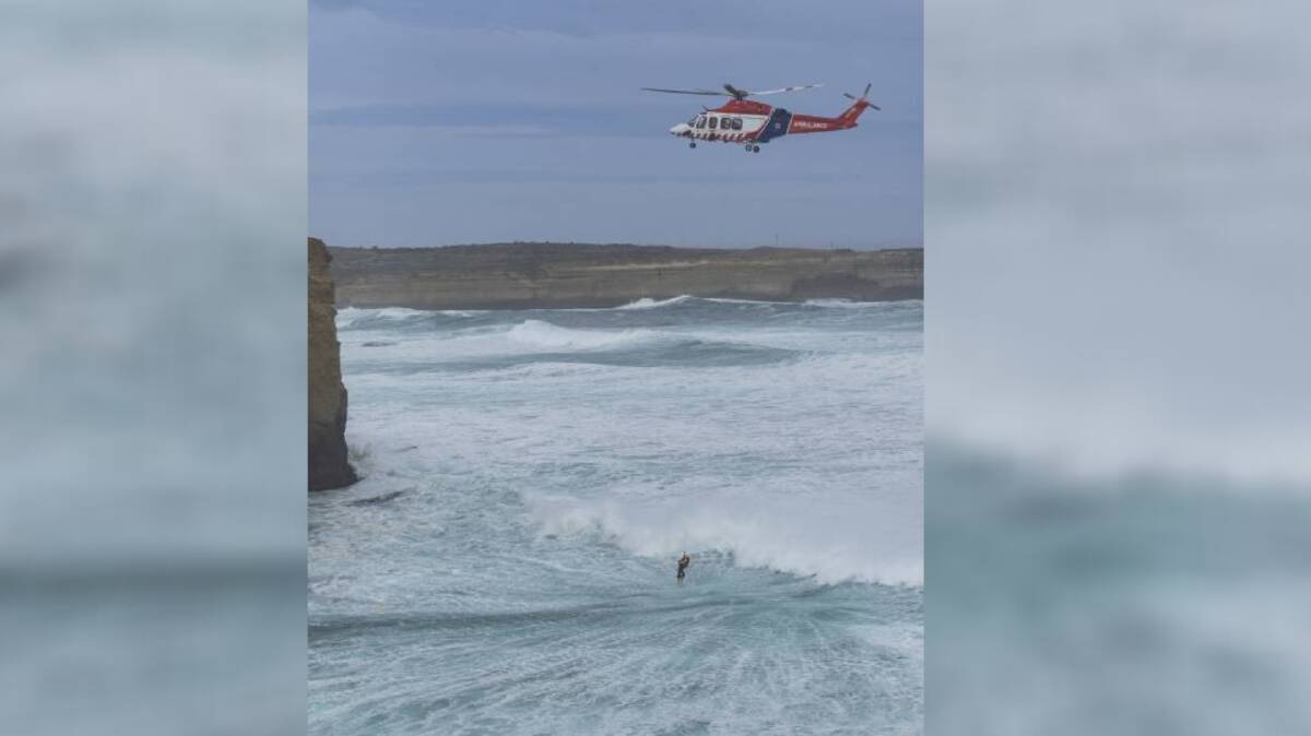 Mission: HEMS4 winches the third lifesaver to safety from the heavy seas near Port Campbell on Sunday where two men died trying to save a tourist. Picture: Ian McCauley