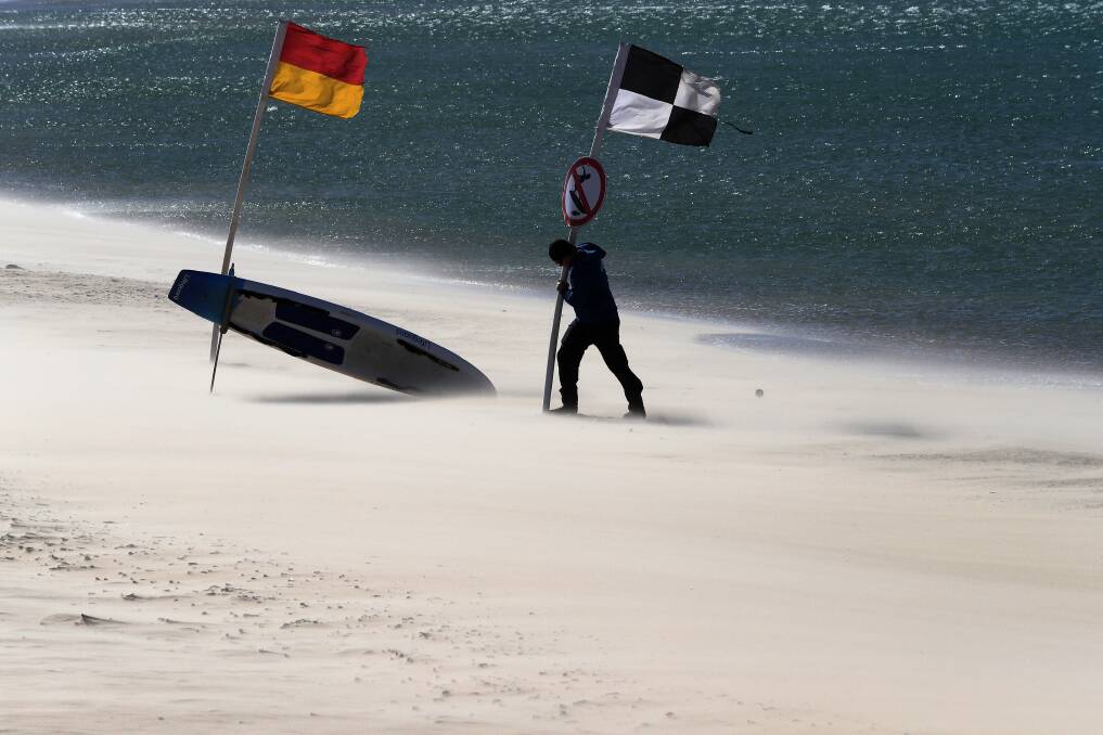 FLAGGING: A lifeguard plants flags back into Nobby's beach amid howling winds on Monday. Conditions were predicted to ease on Tuesday. Picture: Peter Lorimer