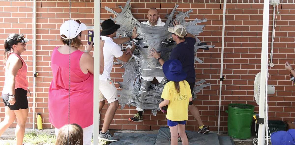 STUCK: Principal Kevin Greaves is duct taped to the wall to raise funds for new playground equipment. Picture: PERRY DUFFIN