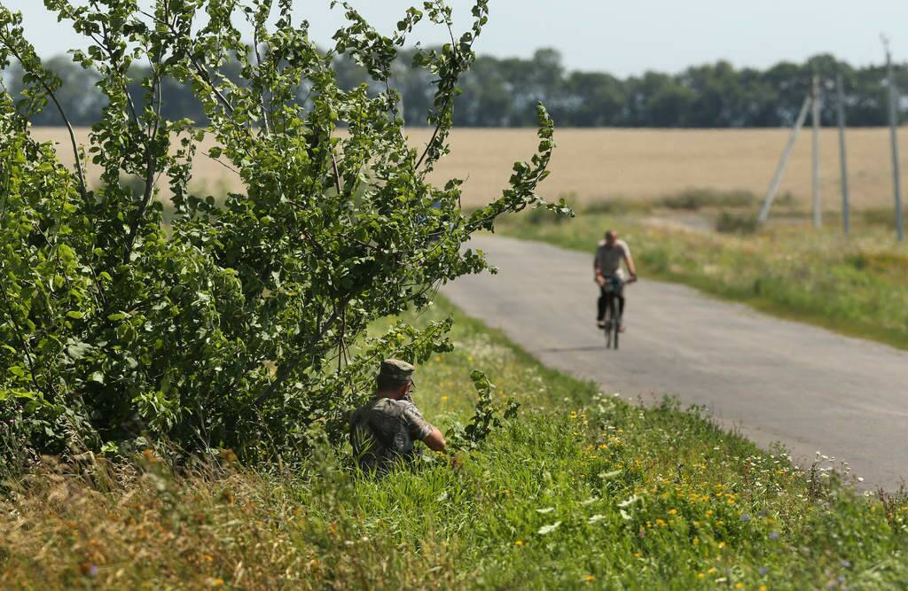 A Pro Russian rebel aims at a man riding a bicycle along the road that borders the MH17 crash site as the Australian and Dutch teams start searching at the MH17 crash site for human remains in order to bring them home. Photo: Kate Geraghty