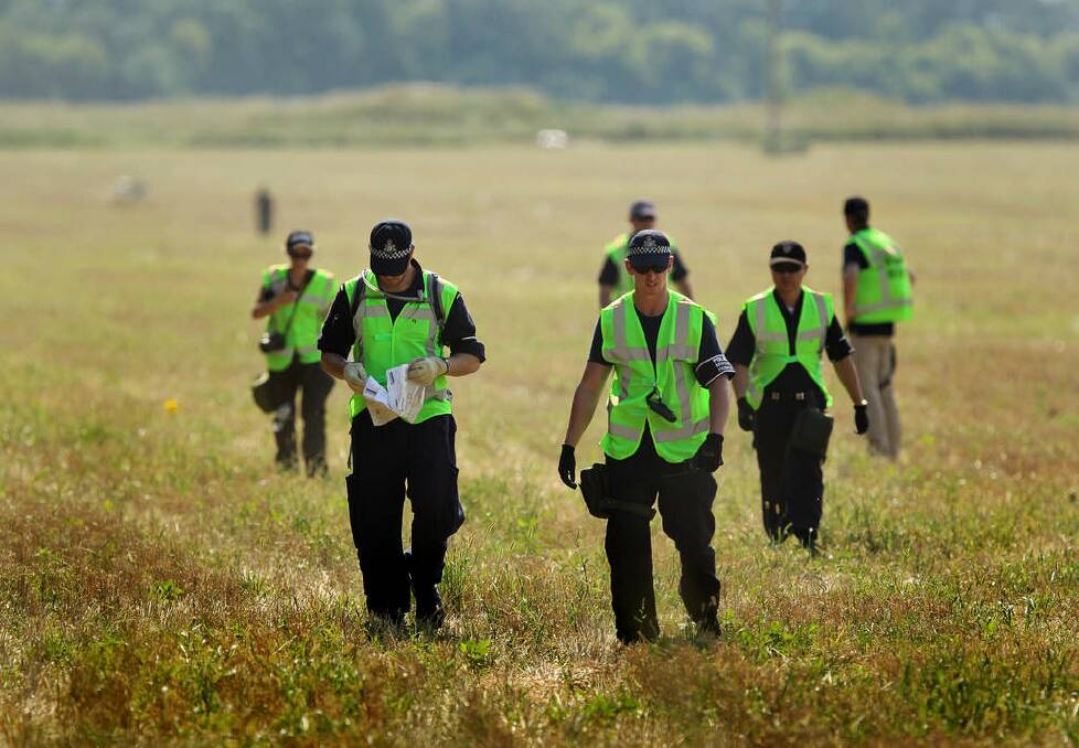 An Australian Federal Police officer (2nd from left) reads Harvey World Travel documents as he walks with a fellow AFP officer (3rd from left) with their  Malaysian and Dutch counterparts return from searching the fields for human remains of passengers from the MH17 crash, on the outskirts of Rassypnoe village. Photo: Kate Geraghty
